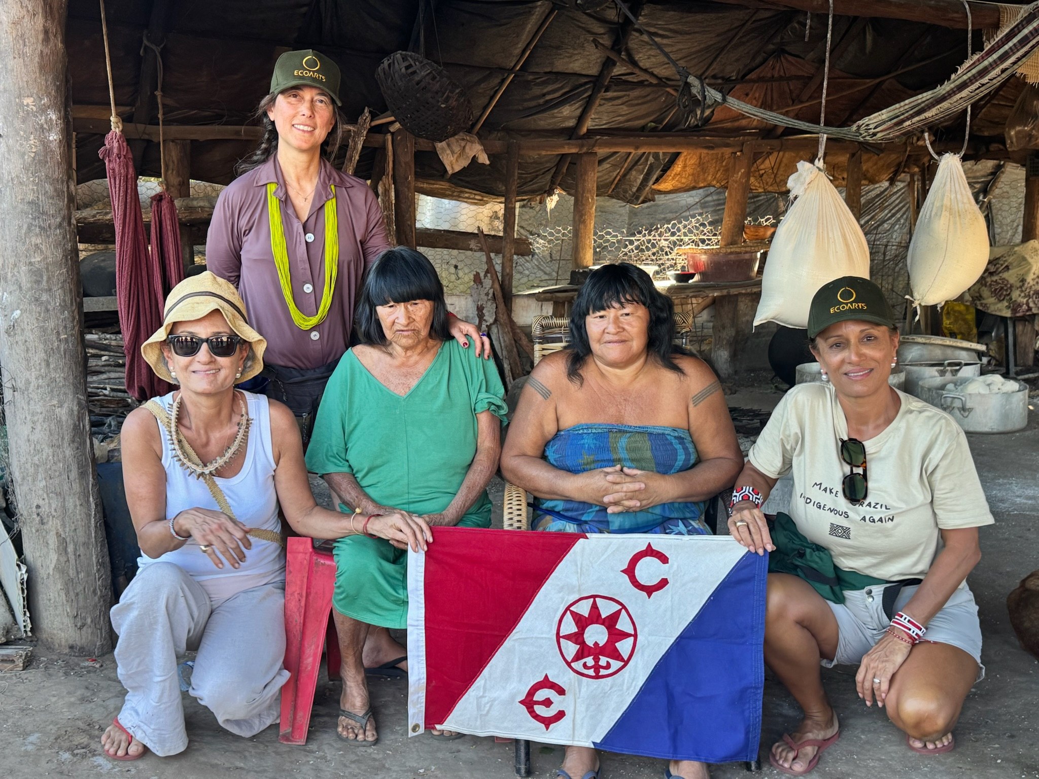 Grupo reunido dentro de maloca com bandeira cerimonial